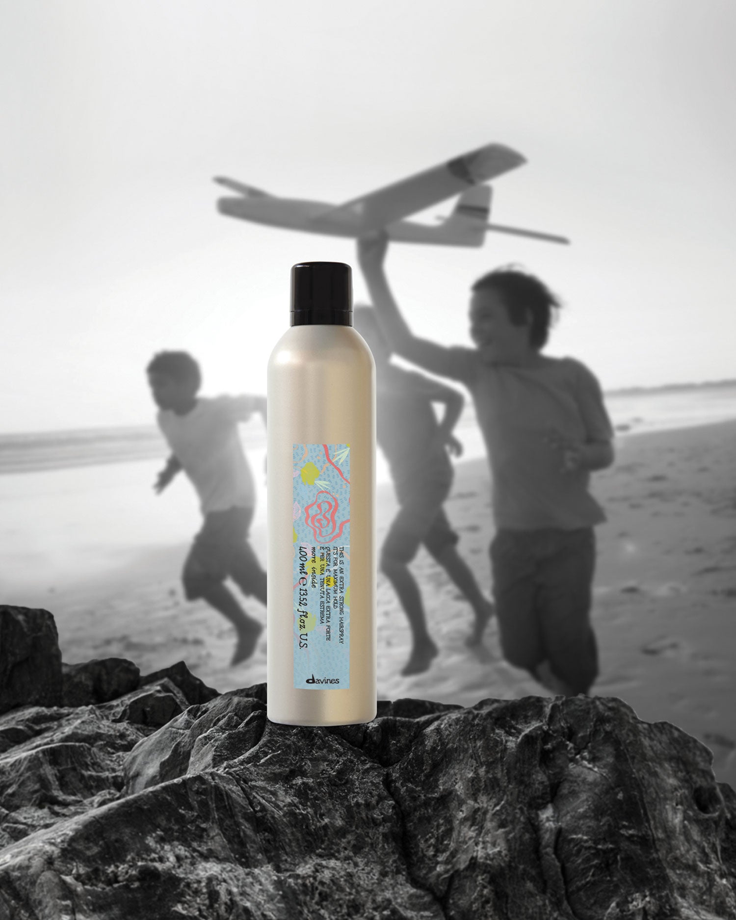 Davines 'SU' family energizing shampoo bottle posed on coastal rocks with children playing at the beach.