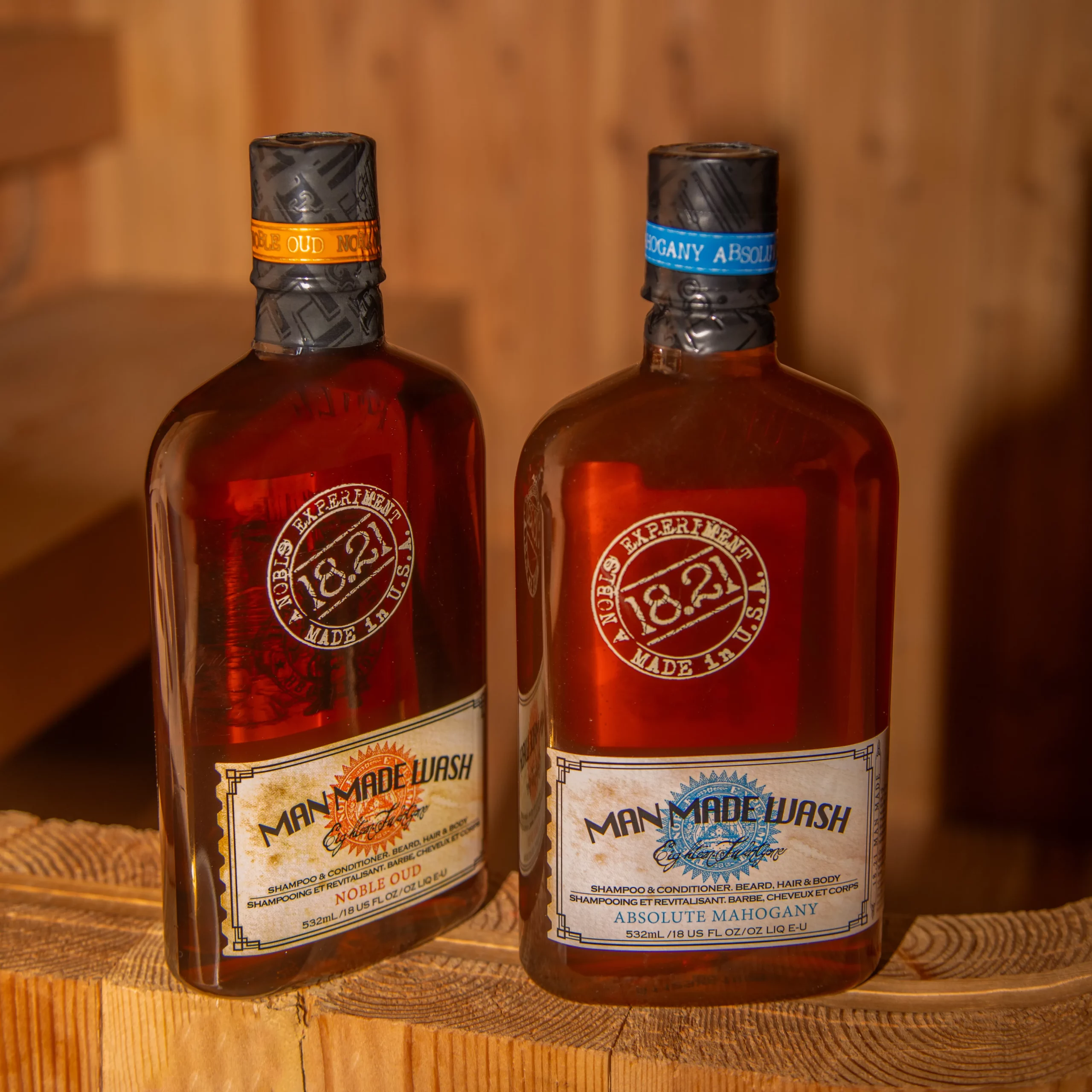 Reuzel 'Man Made Wash' Original and 'Absolute Mahogany' body wash bottles on a wooden barrel.