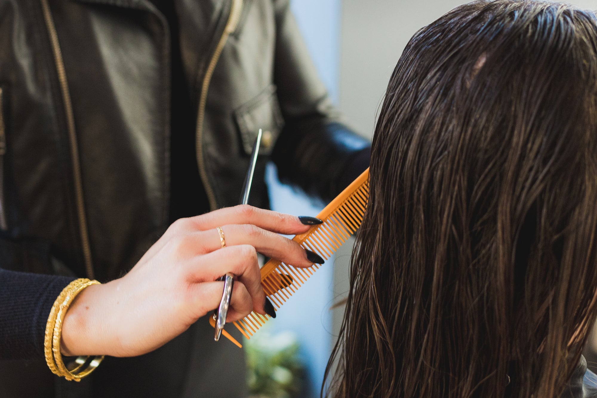 Professional styling in action: a stylist's hands comb through a client's wet dark hair with an orange comb.
