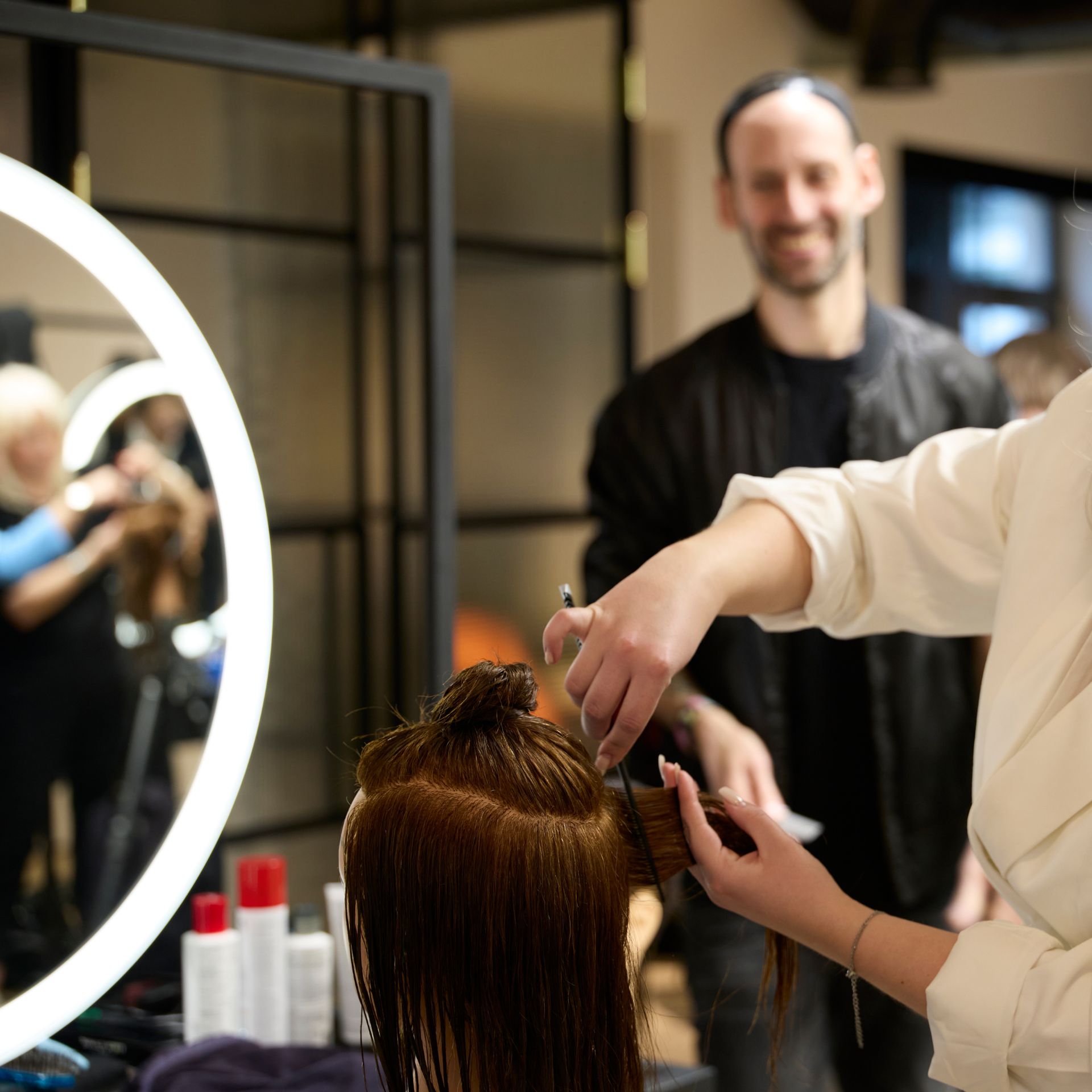 A hairdresser styling a client's hair in a partner salon lit by a ring-light mirror.